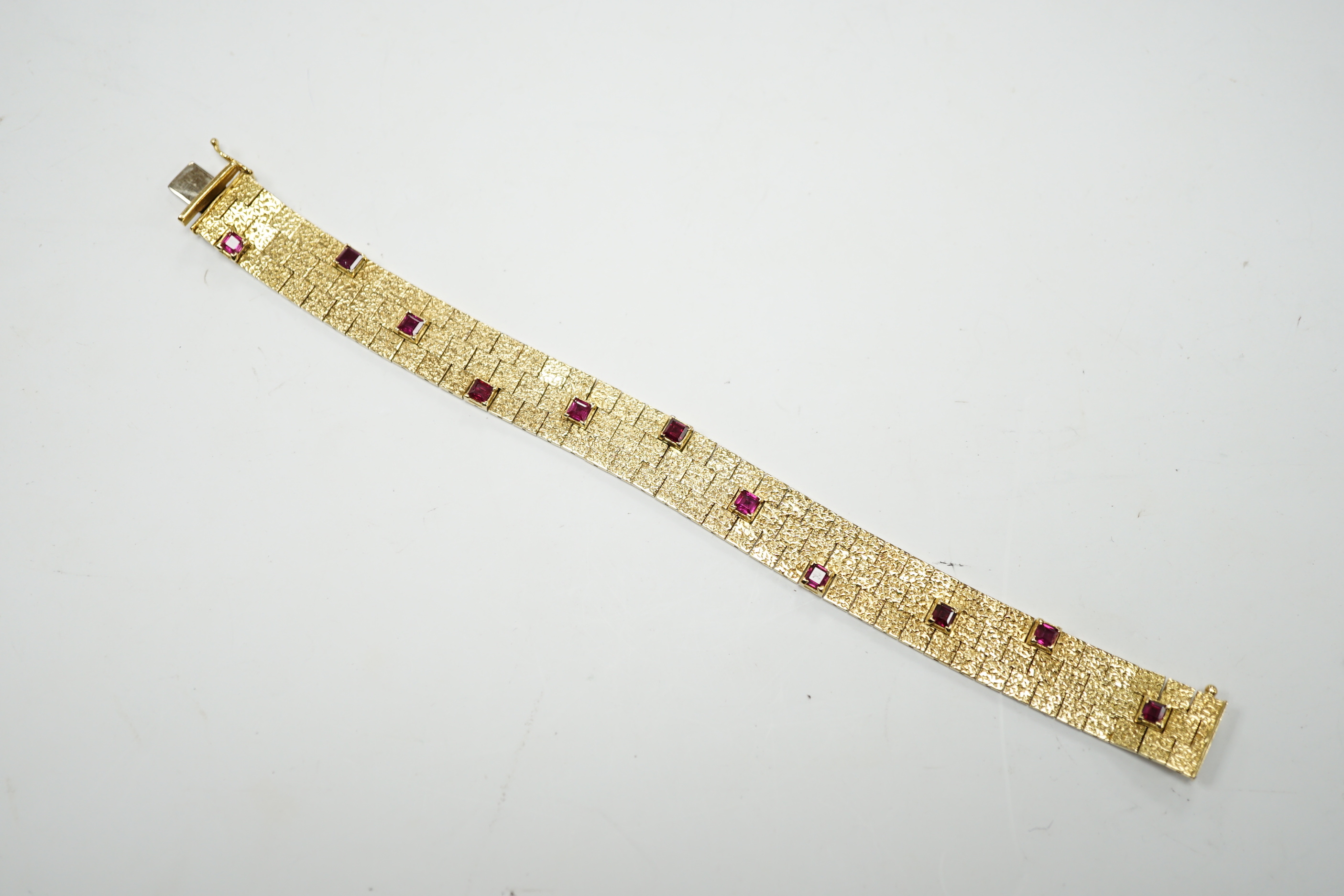 A textured yellow metal and eleven stone square cut ruby set bracelet, 16.5cm, gross weight 36.8 grams.